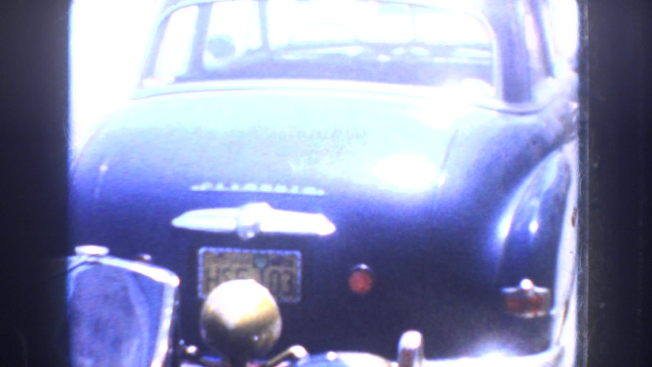1952 California home-movie frame showing the rear of a dark blue classic car partly obscured by a dark interior frame.