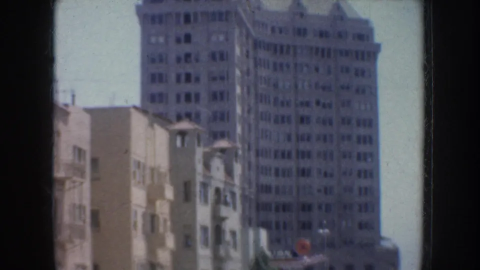 1952 California urban frame showing tall buildings, a partial parked car, and street activity bordered by dark 8mm frame edges.