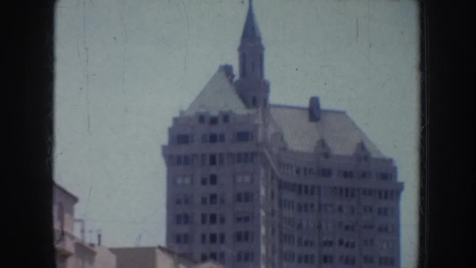1952 California frame of an ornate city building with a pointed spire and surrounding urban rooftops.