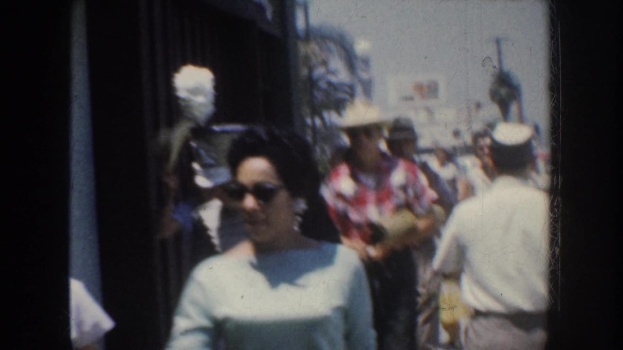 Woman in sunglasses walks toward the camera on a crowded sidewalk.
