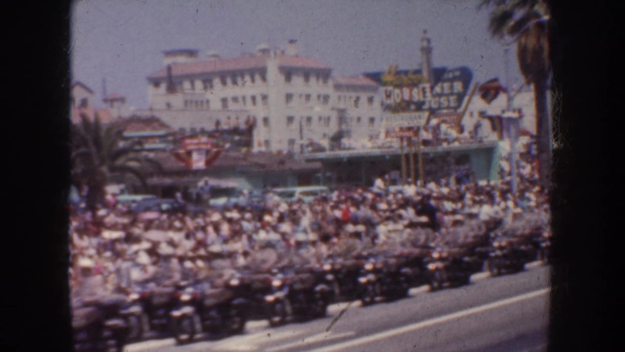 A 1952 California street scene shows rows of motorcycles and many spectators gathered outside commercial buildings with palm trees and signage visible.