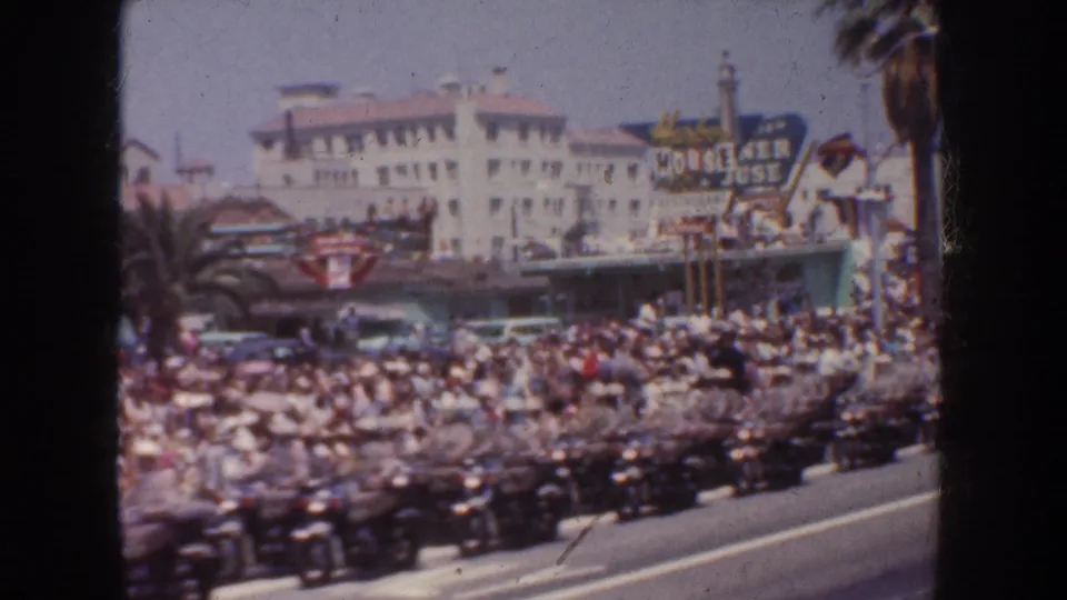 A 1952 California street scene shows rows of motorcycles and many spectators gathered outside commercial buildings with palm trees and signage visible.