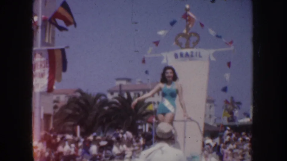1952 California parade view of the Brazil float, showing the performer on the platform, pennant flags, palm trees, and spectators.