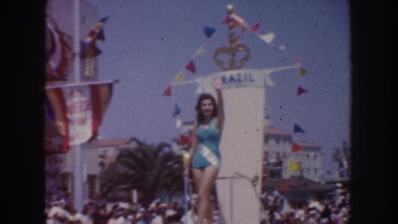 1952 California home-movie frame of the Brazil parade float, with the sash-wearing woman posing above a crowded street.