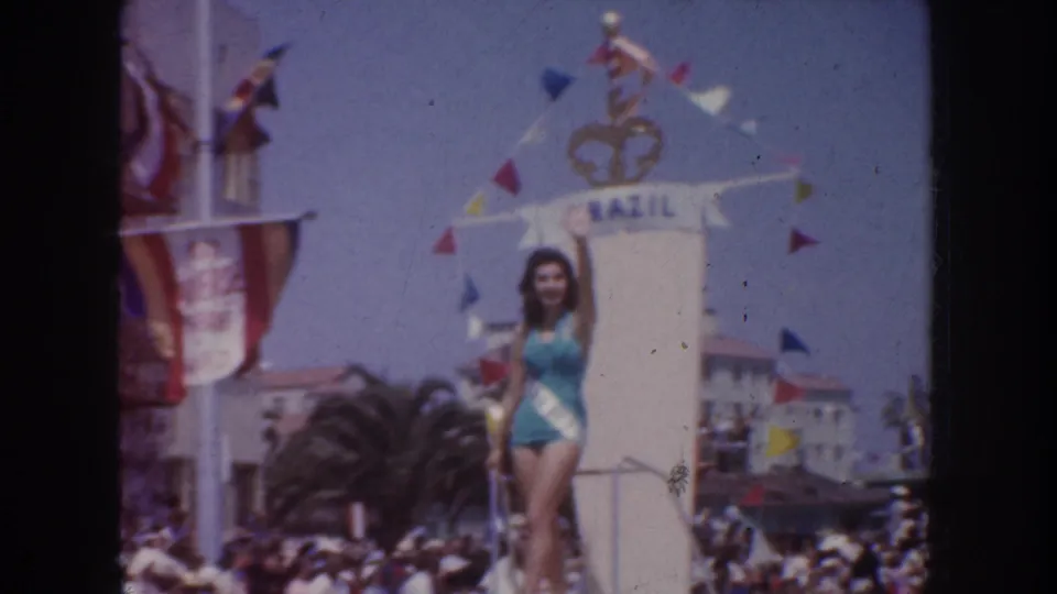 1952 California home-movie frame of the Brazil parade float, with the sash-wearing woman posing above a crowded street.