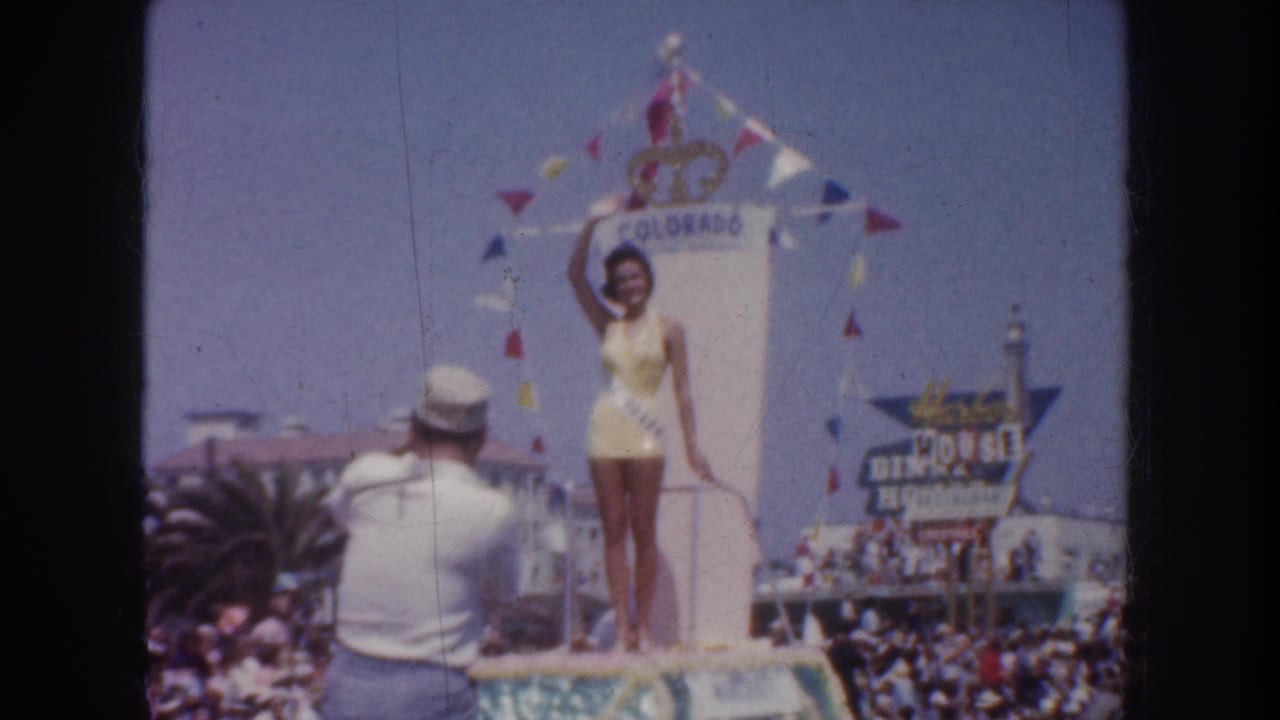 1952 California home-movie frame showing a beauty queen on a float labeled Colorado, waving above spectators and bunting.