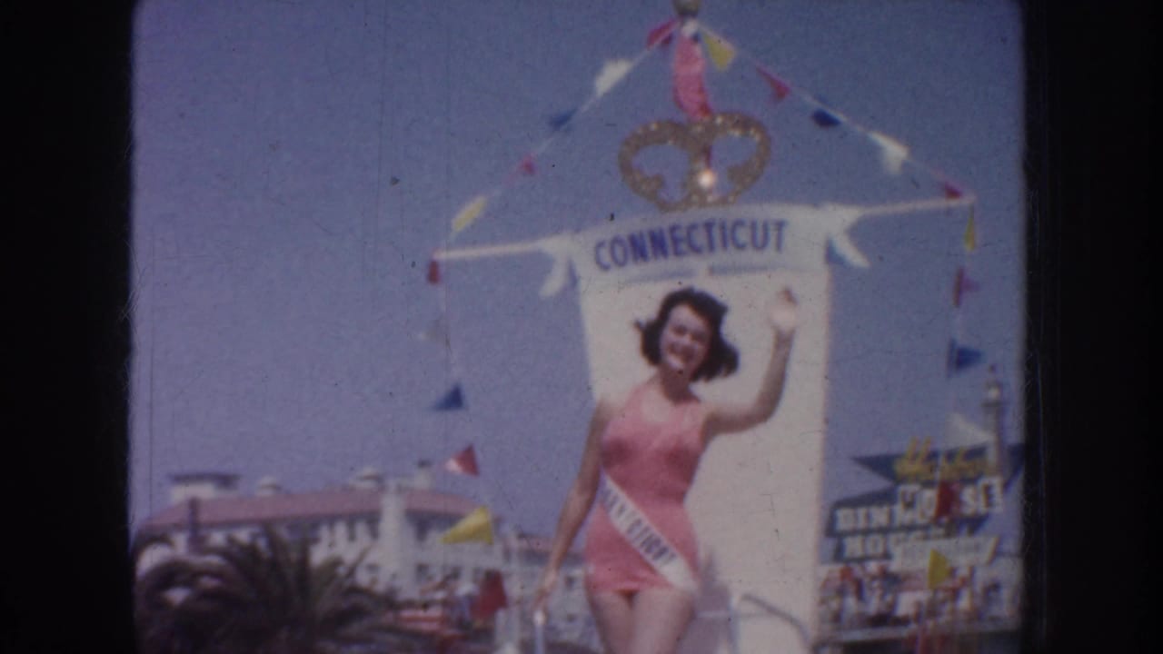 1952 California home-movie frame showing a waving contestant on a float labeled Connecticut, with flags and street spectators visible.