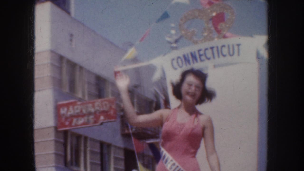 1952 California parade frame showing a sash-wearing woman in pink waving near a Connecticut banner and storefront signage.