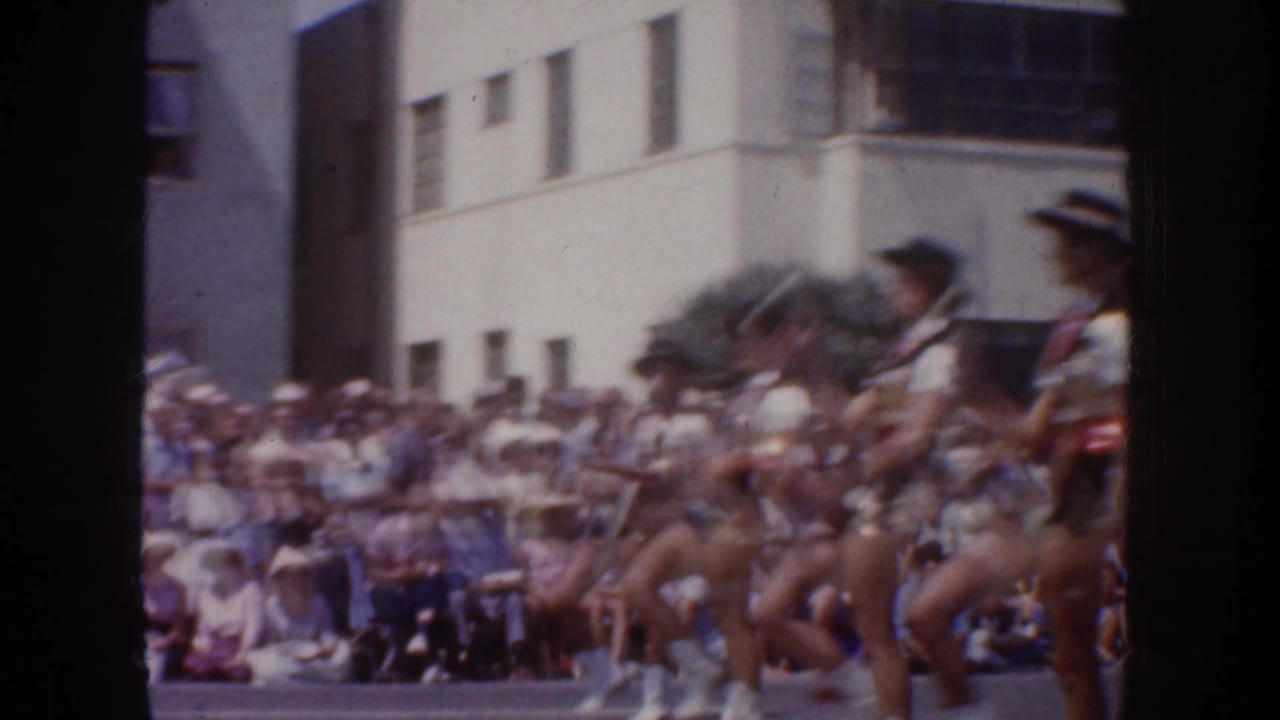 Female dancers perform in formation before a large crowd on a city street.