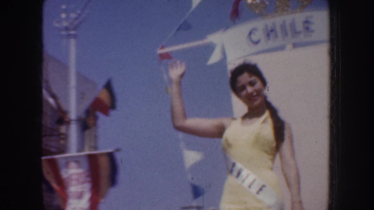 A sash-wearing woman in yellow waves beside a Chile banner in 1952 California parade home-movie footage.