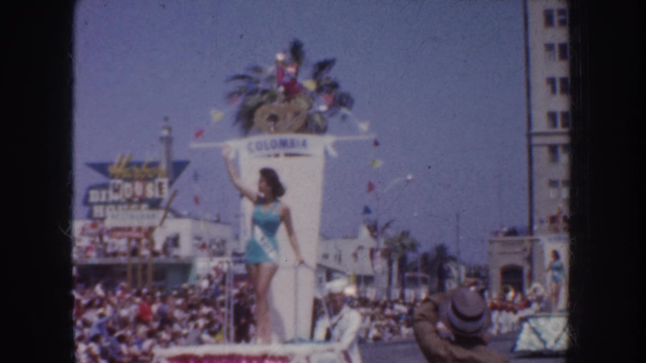 A wide 1952 California parade view shows a swimsuit contestant on a float, a crowd, palm trees, and Columbia lettering.