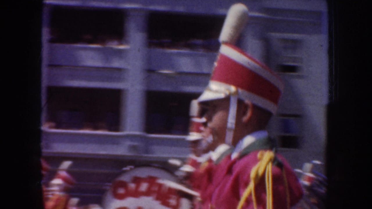 1952 California parade view of a uniformed band member in red and white marching past a multi-story street building.