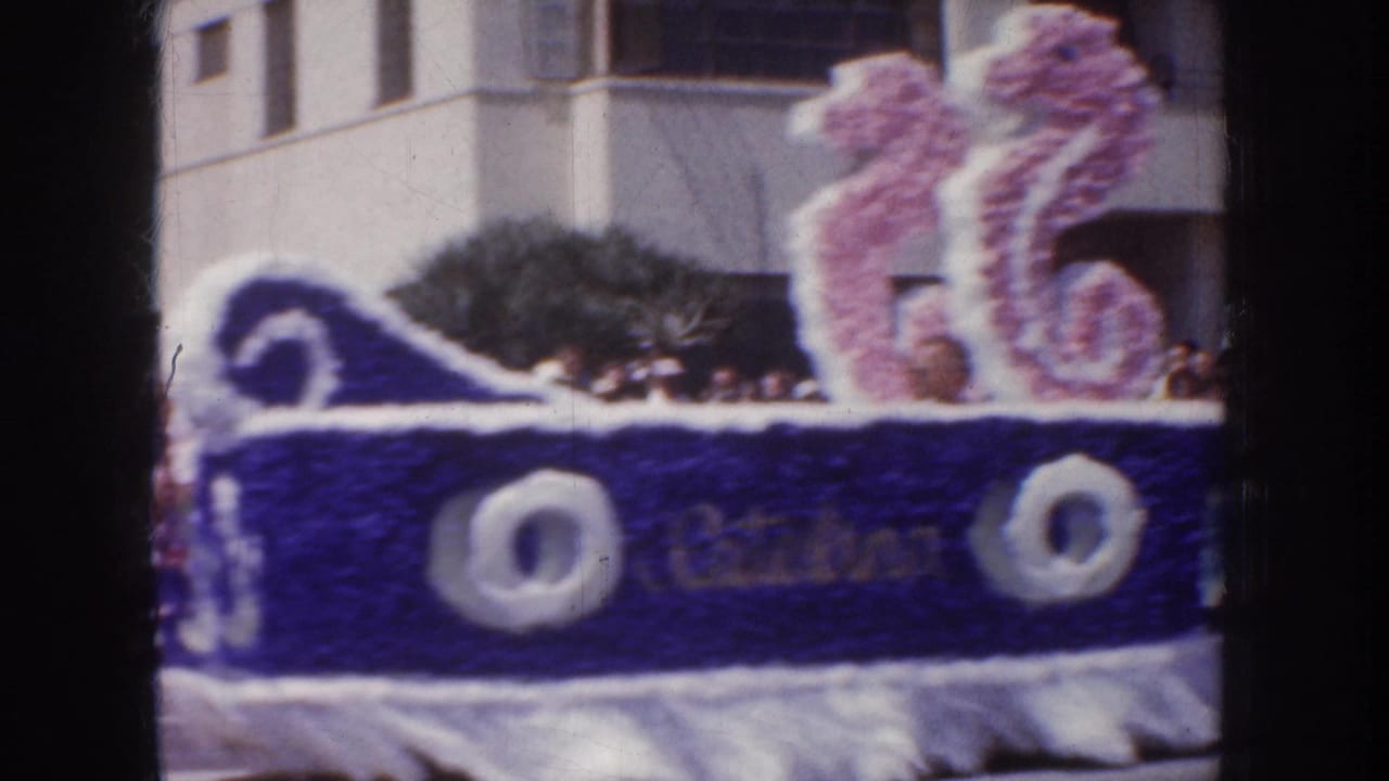 1952 California parade frame showing a decorated float with a pink seahorse prop, blue trim, spectators, and nearby buildings.