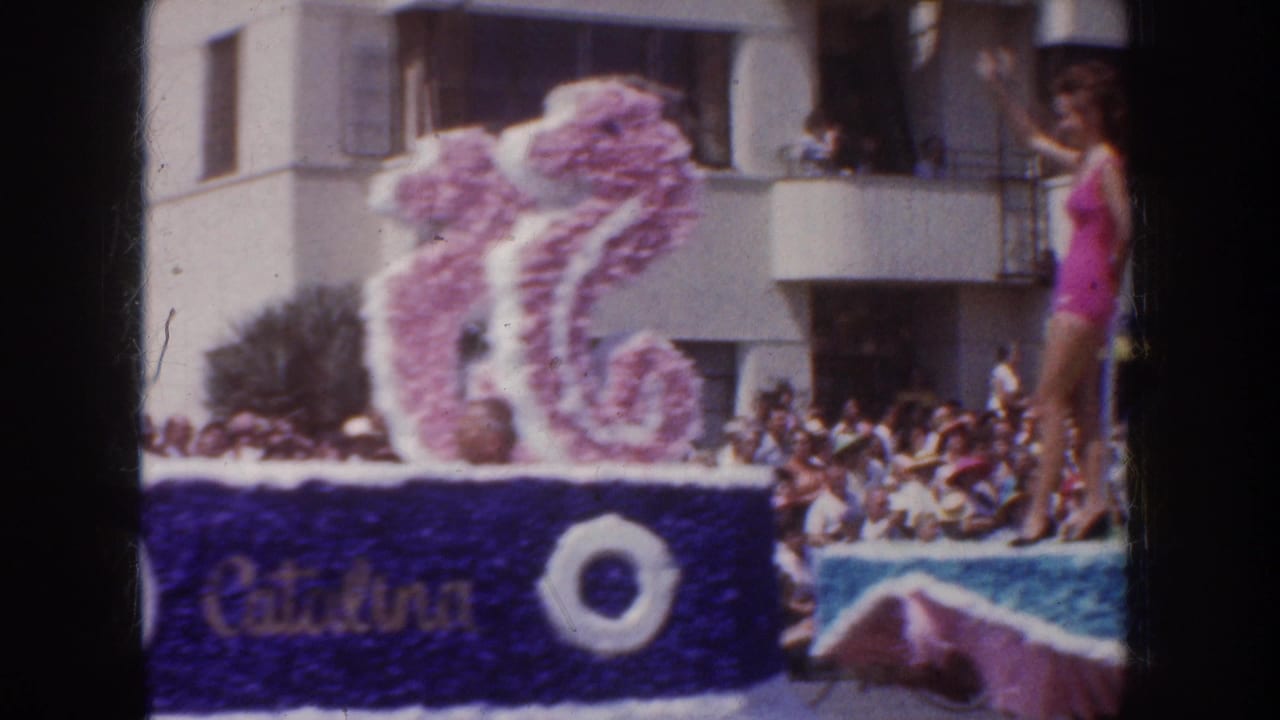 Floral parade float with Catalina text and a woman in a pink swimsuit waving to spectators.