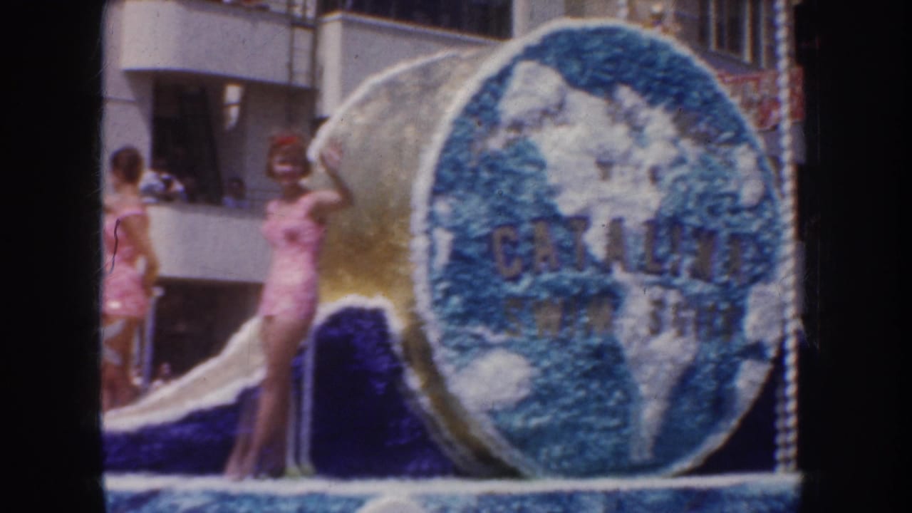 Swimsuit-clad women stand on a California parade float beside a large floral globe panel marked Catalina.