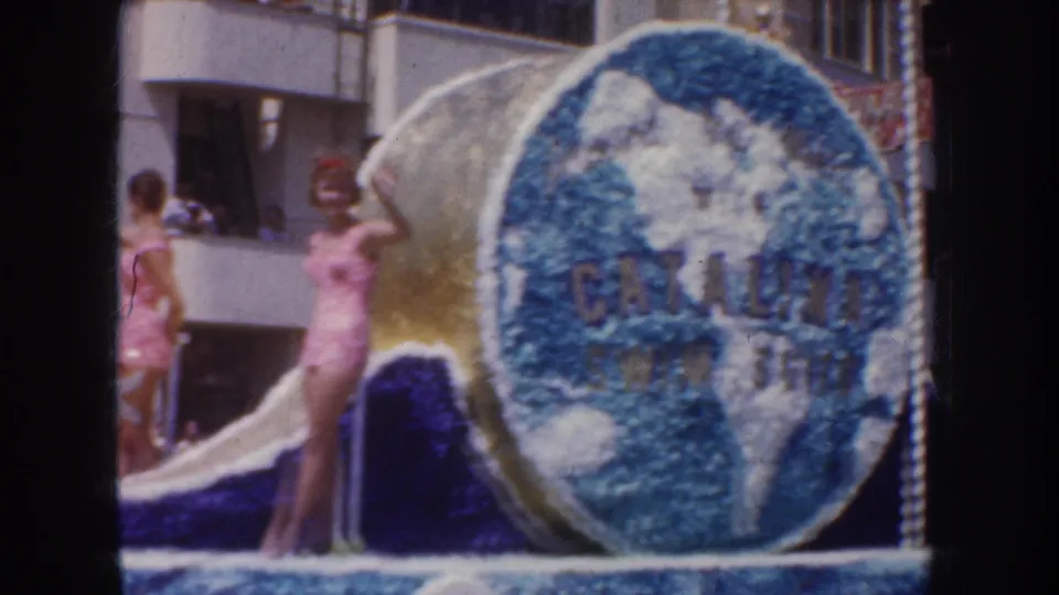 Swimsuit-clad women stand on a California parade float beside a large floral globe panel marked Catalina.