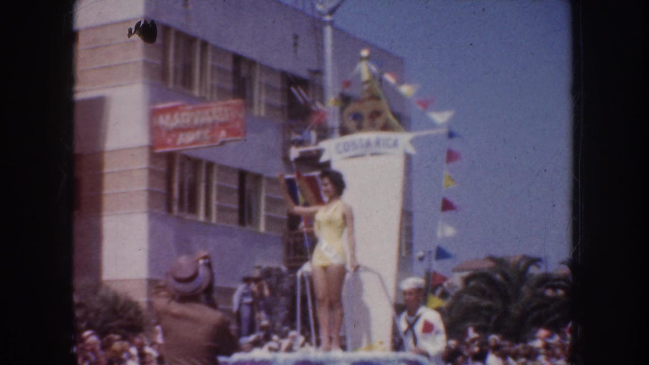 1952 California 8mm frame showing a woman in a yellow swimsuit on a COSTA RICA parade float with pennants, spectators, and a HARVARD sign nearby.
