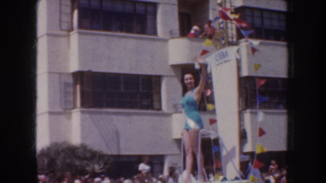 1952 California parade frame with a woman in a blue swimsuit waving from a decorated float below balcony spectators and colorful pennants.