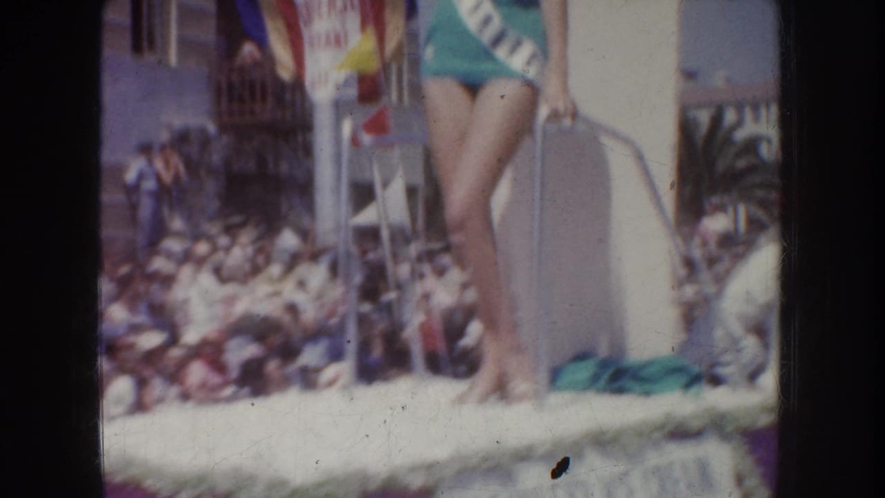 Home-movie frame from the 1952 California parade showing the pageant participant on the float above a crowded street.