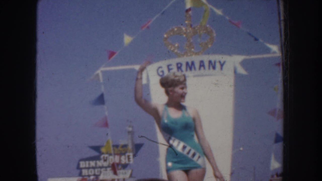 Contestant in turquoise swimsuit waves in front of a Germany sign and crown emblem.