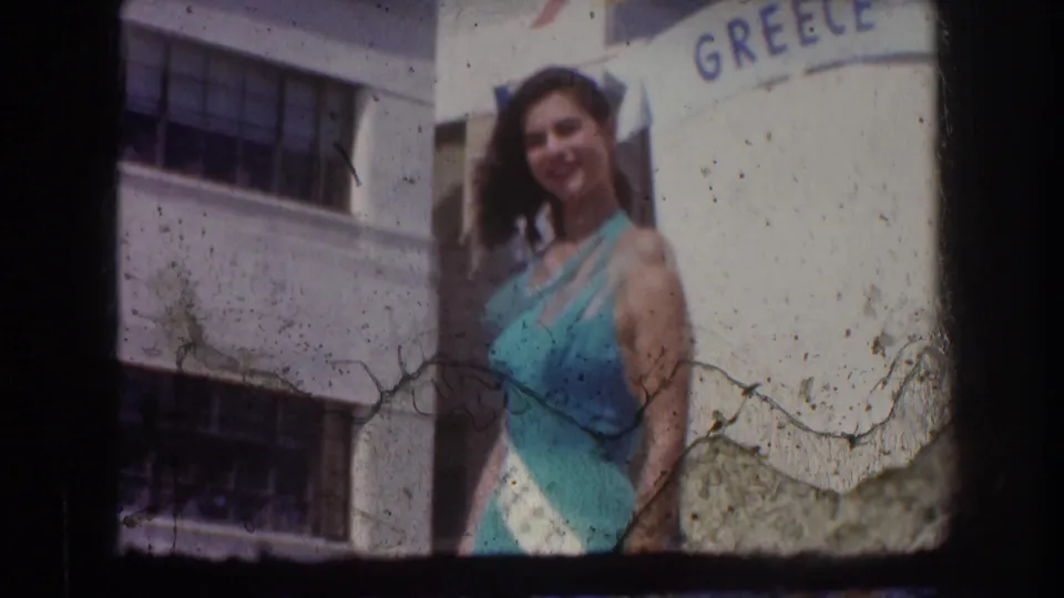 Final frame shows the Grecian pageant queen smiling near the GREECE float sign, with 8mm dirt and emulsion marks visible.
