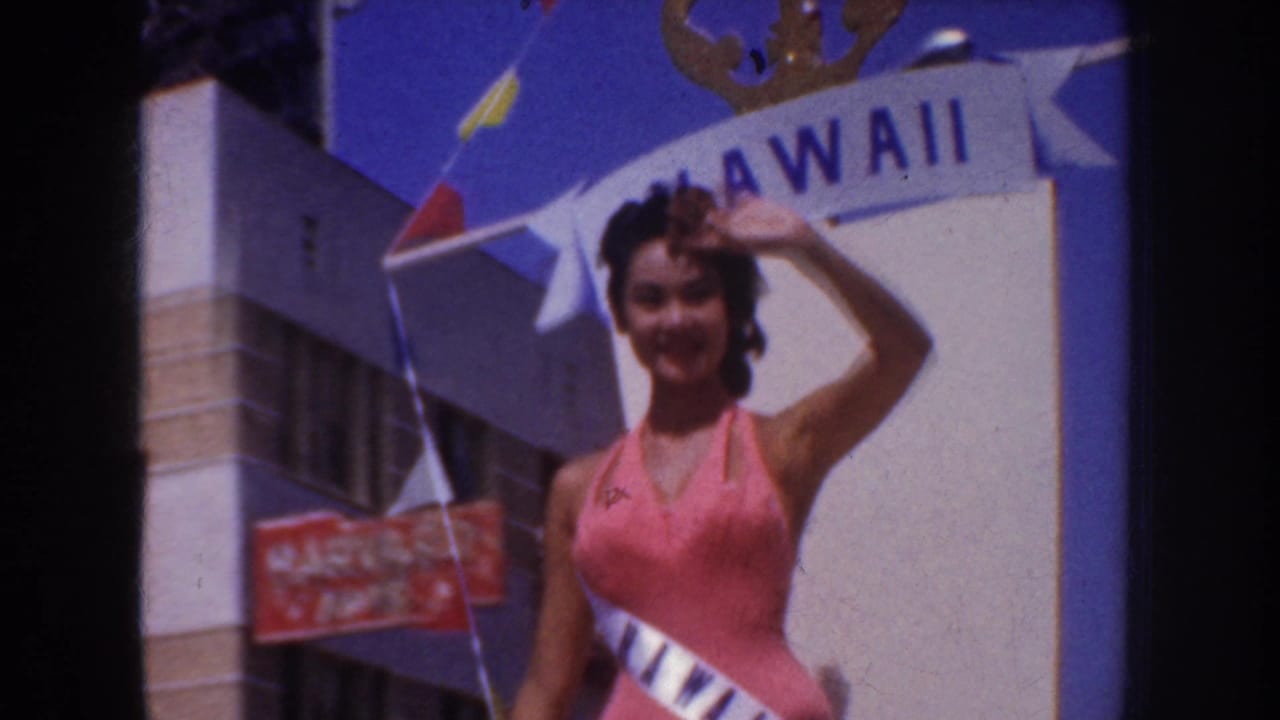 Smiling woman in pink waves beneath a Hawaii banner with flags nearby.