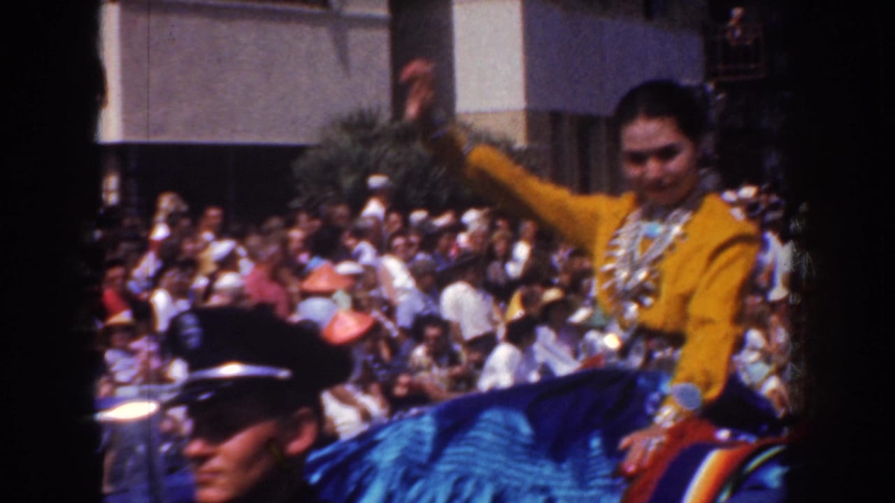 Woman in yellow costume waves from a parade vehicle before a large crowd.