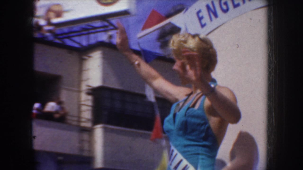 Blonde woman in a blue swimsuit waves near an England sign and flags.