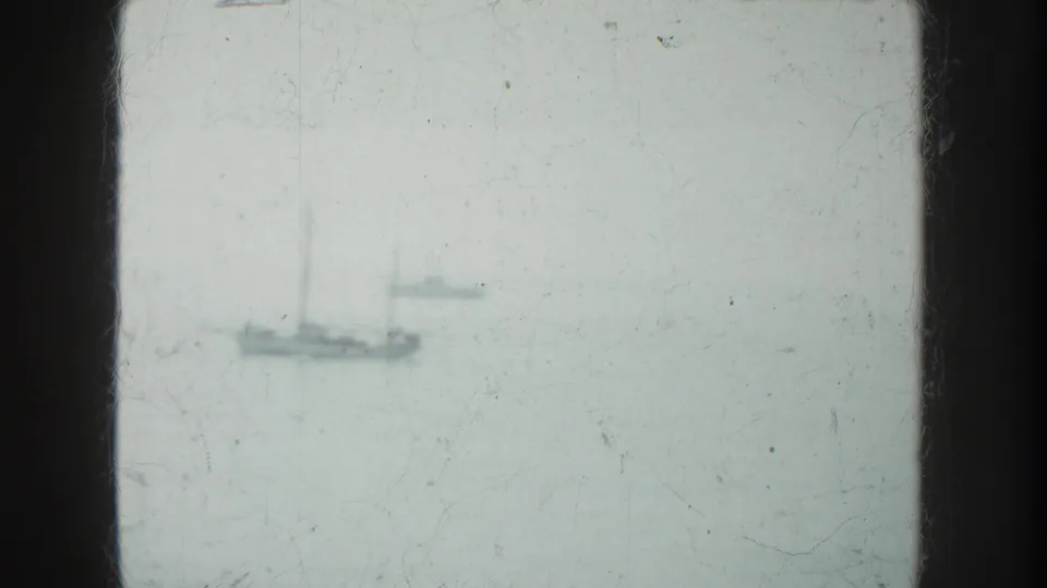 Soft 1952 8mm view of distant ships or boats on pale water, framed by dark film edges and visible surface wear.