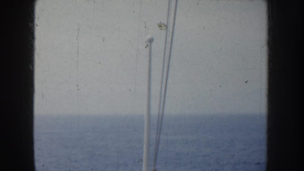 A mostly empty view of ocean and sky from the ship, framed by dark film or window edges and a white vertical pole.