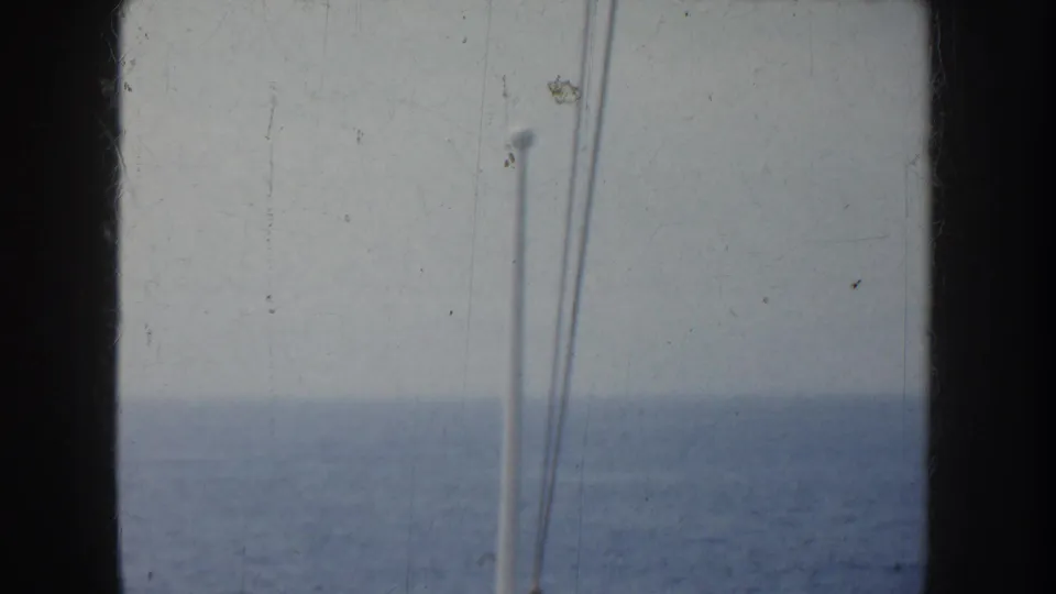 A mostly empty view of ocean and sky from the ship, framed by dark film or window edges and a white vertical pole.