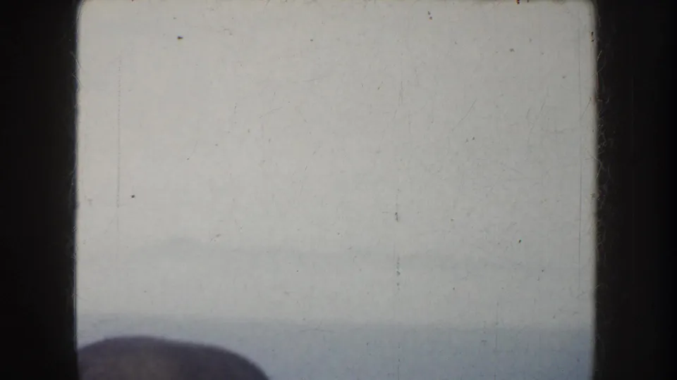 A soft, overexposed home-movie frame of sea and sky, with a dark partial shape entering along the lower edge.