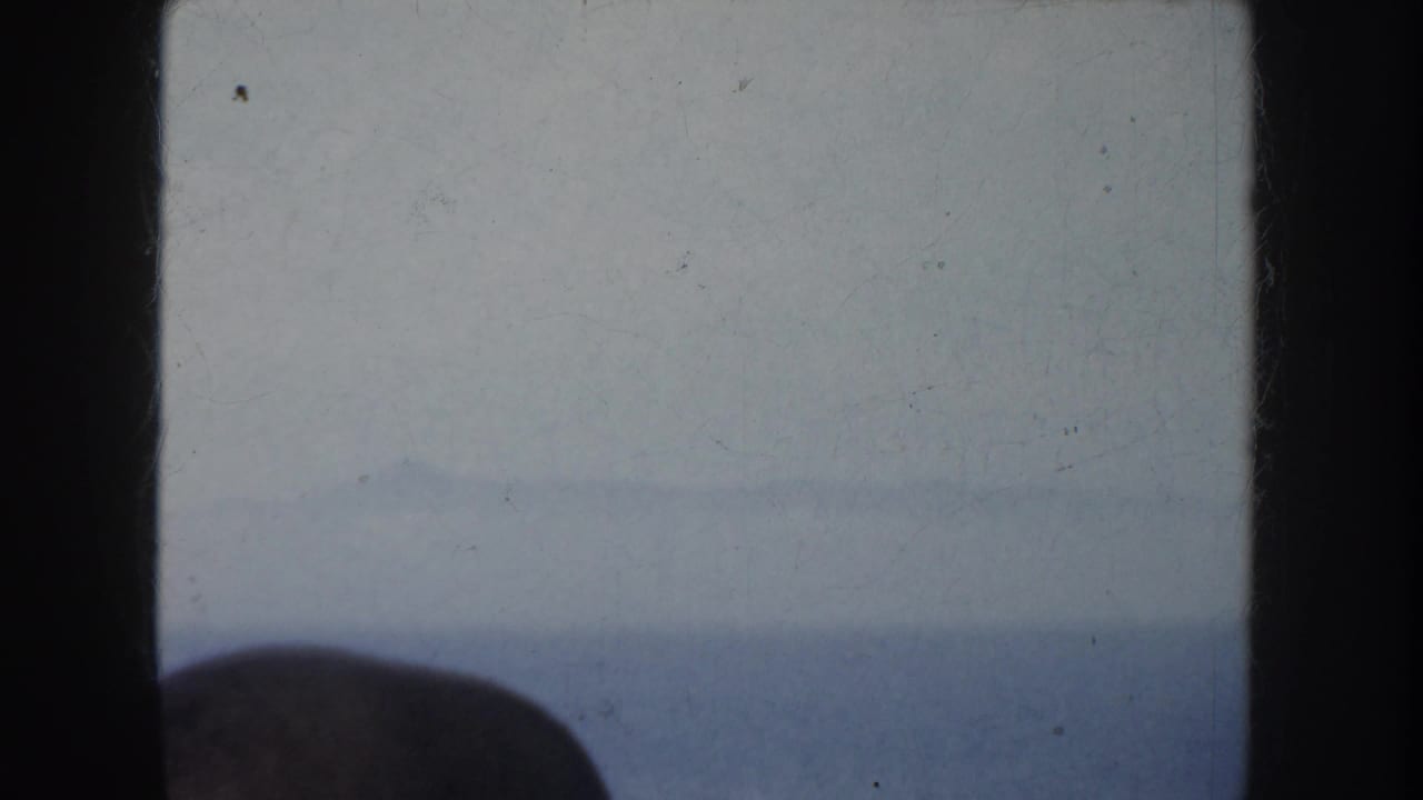 1952 California 8mm frame showing a soft, hazy ocean horizon from a boat or window-like vantage, with dark gate borders and a foreground silhouette.