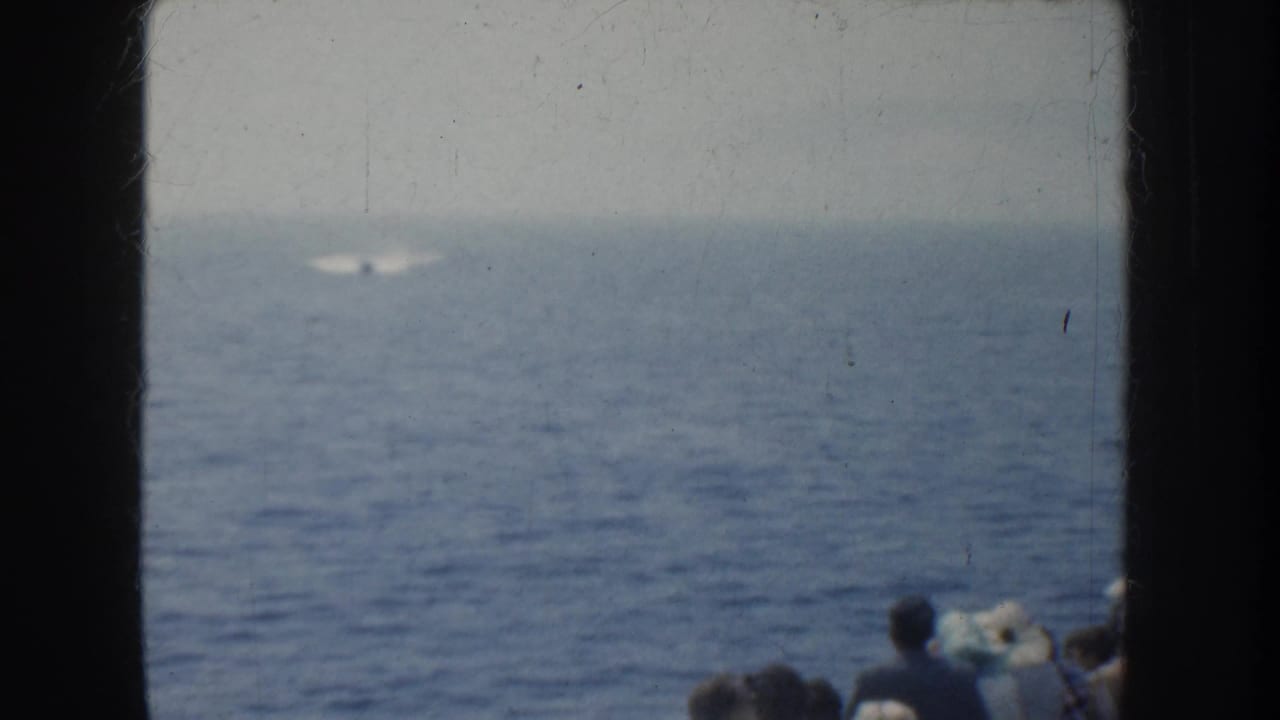 1952 California home-movie frame of open ocean with a distant bright object or wake, while boat passengers appear partly at the lower right edge.