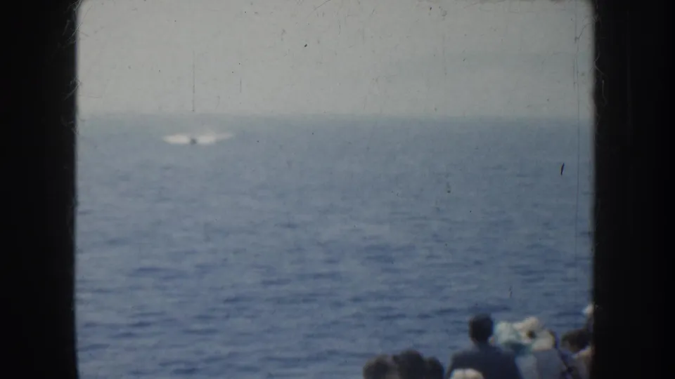 1952 California home-movie frame of open ocean with a distant bright object or wake, while boat passengers appear partly at the lower right edge.