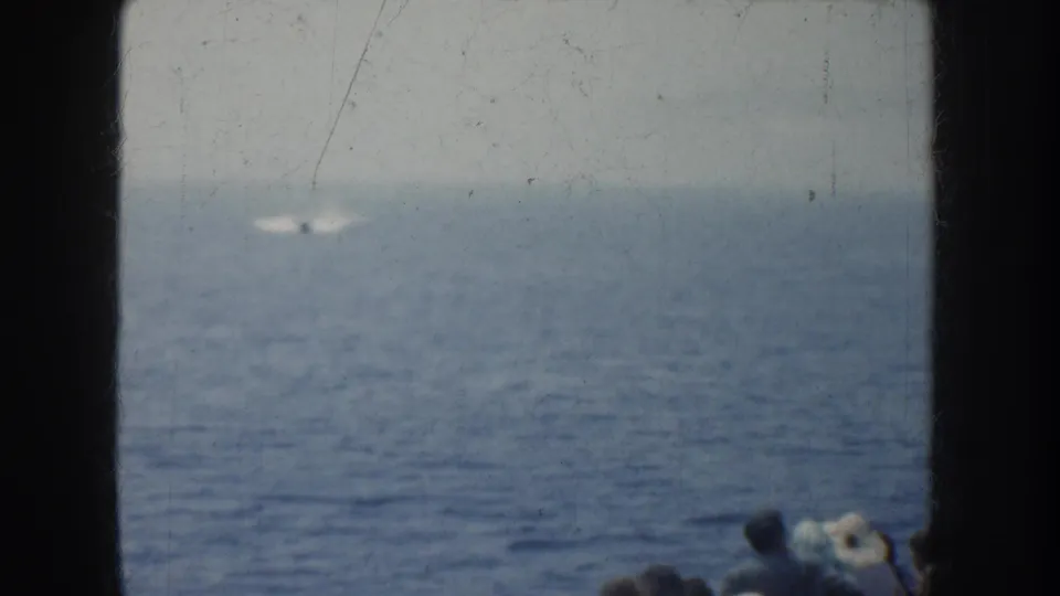 1952 California 8mm view of a distant white object or wake on the water, with boat passengers partly visible in the lower right corner.