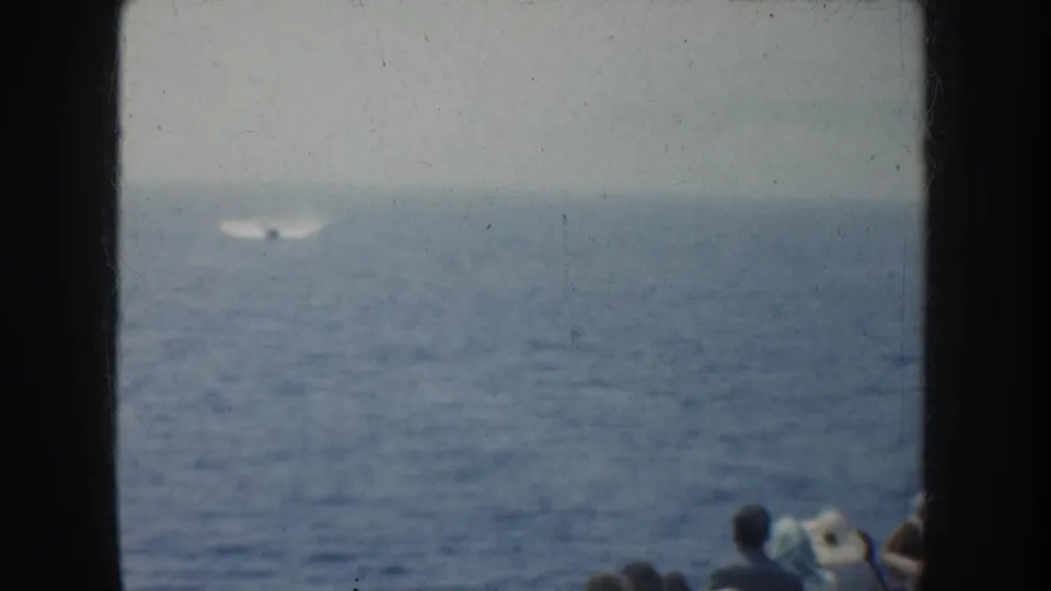1952 California home-movie frame showing a small dark object with pale wake on the ocean, watched by partially visible boat passengers.