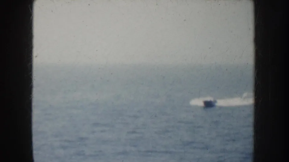 1952 California home-movie frame showing a small speedboat and white wake seen through a dark ship window or opening.