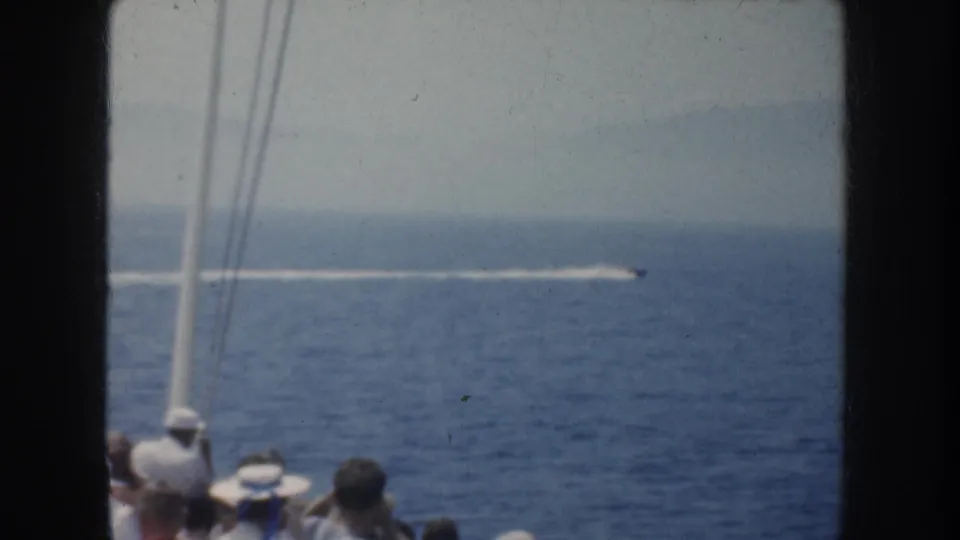 1952 California shipboard frame with rigging, seated spectators, and a distant speedboat trail cutting across the water.