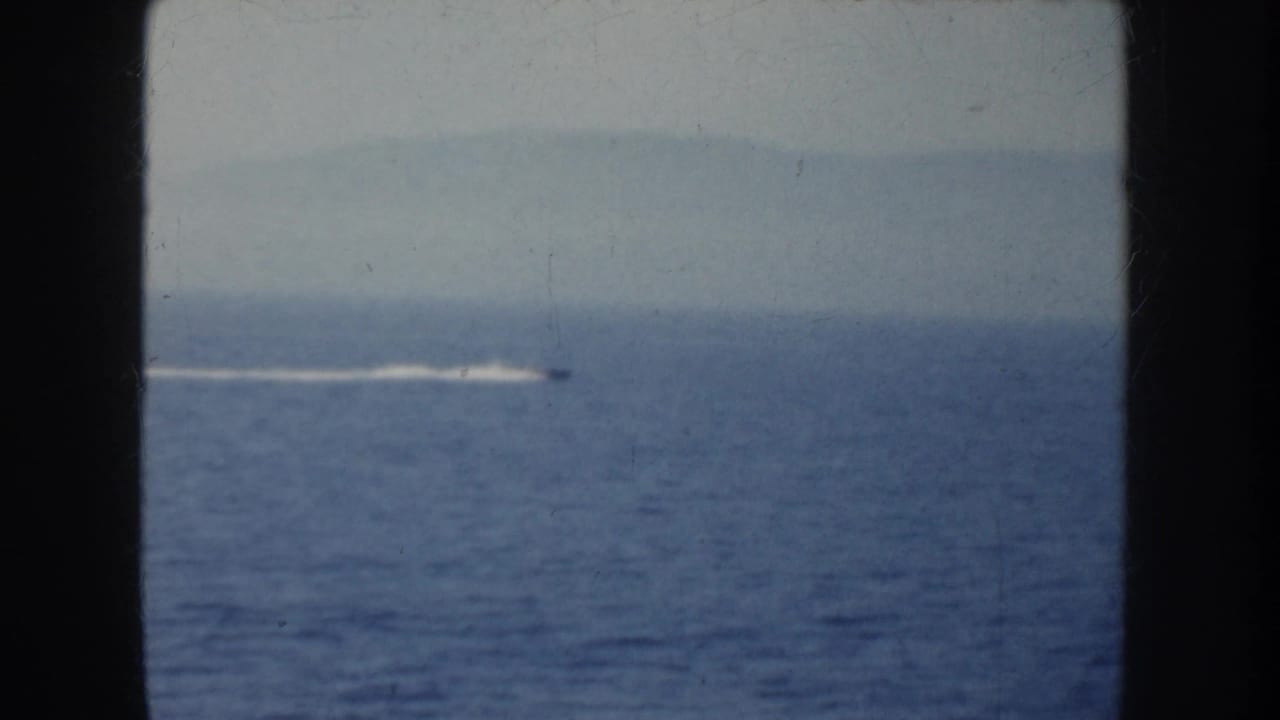 Small speedboat and white wake on open water behind dark framing.