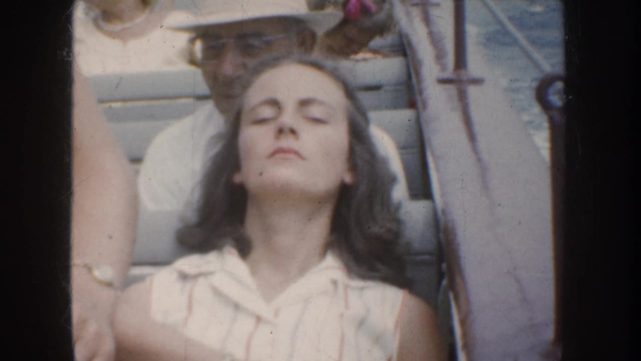 1952 California home-movie frame of a young woman resting with eyes closed on a boat, with a man in a hat behind her.