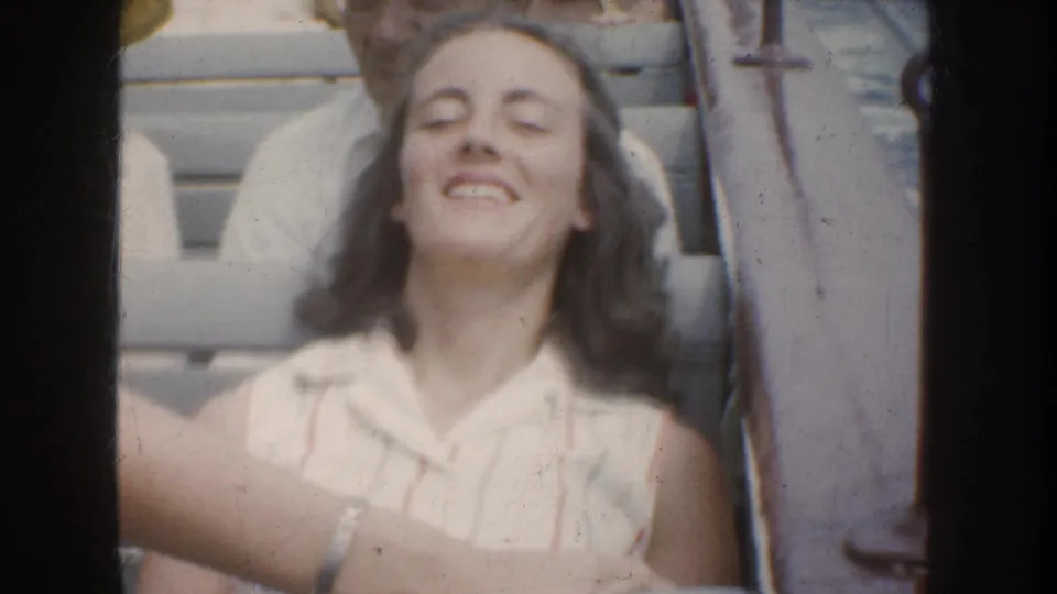 1952 California home-movie frame of a young woman smiling with eyes closed on a boat, with another passenger partly visible behind her.