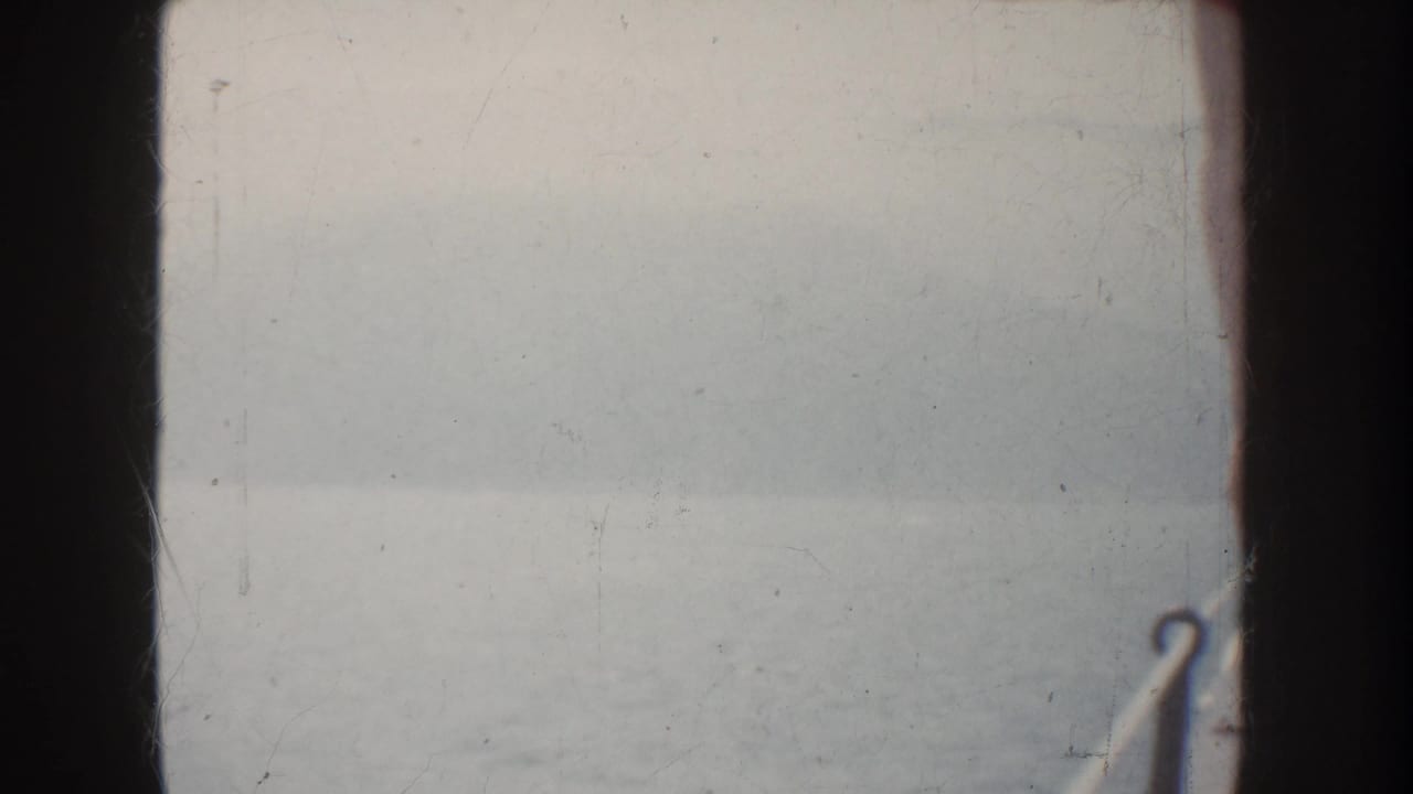 1952 California 8mm frame showing fog over calm water, a hazy distant shoreline, and dark vertical boat framing.