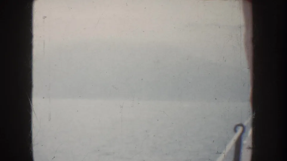 1952 California 8mm frame showing fog over calm water, a hazy distant shoreline, and dark vertical boat framing.