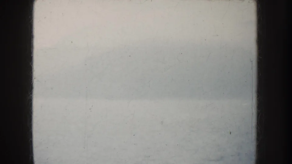 Foggy California water view from an 8mm home movie, with calm surface, faint landform, and dark boat structure at the sides.