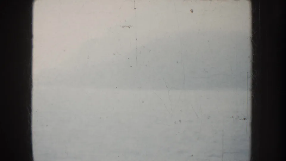 1952 California boat-view frame with misty water, faint shoreline, dark vertical edges, and a small rail or hook visible near the horizon.