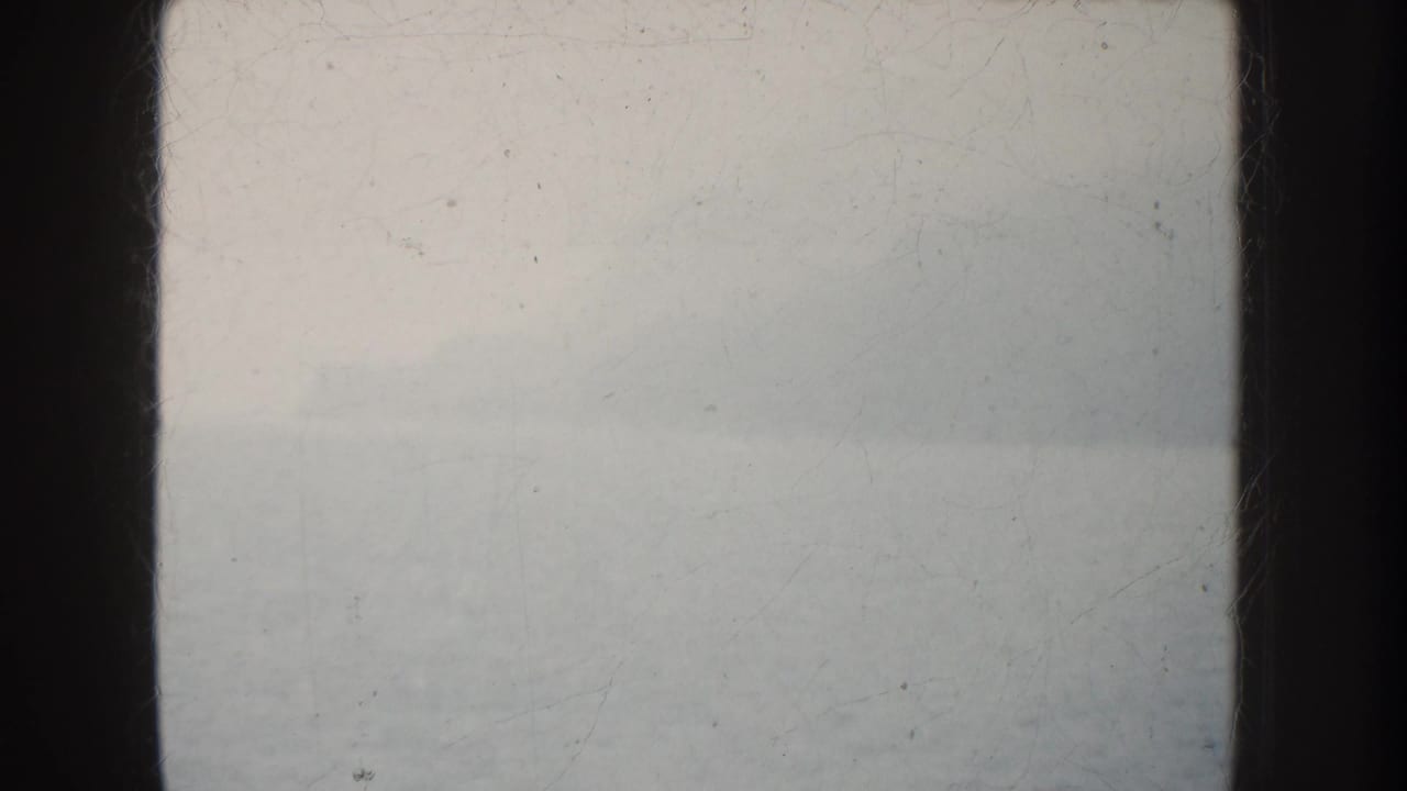 Overexposed 1952 California 8mm frame showing a pale ocean horizon through dark vertical framing, with film scratches visible.