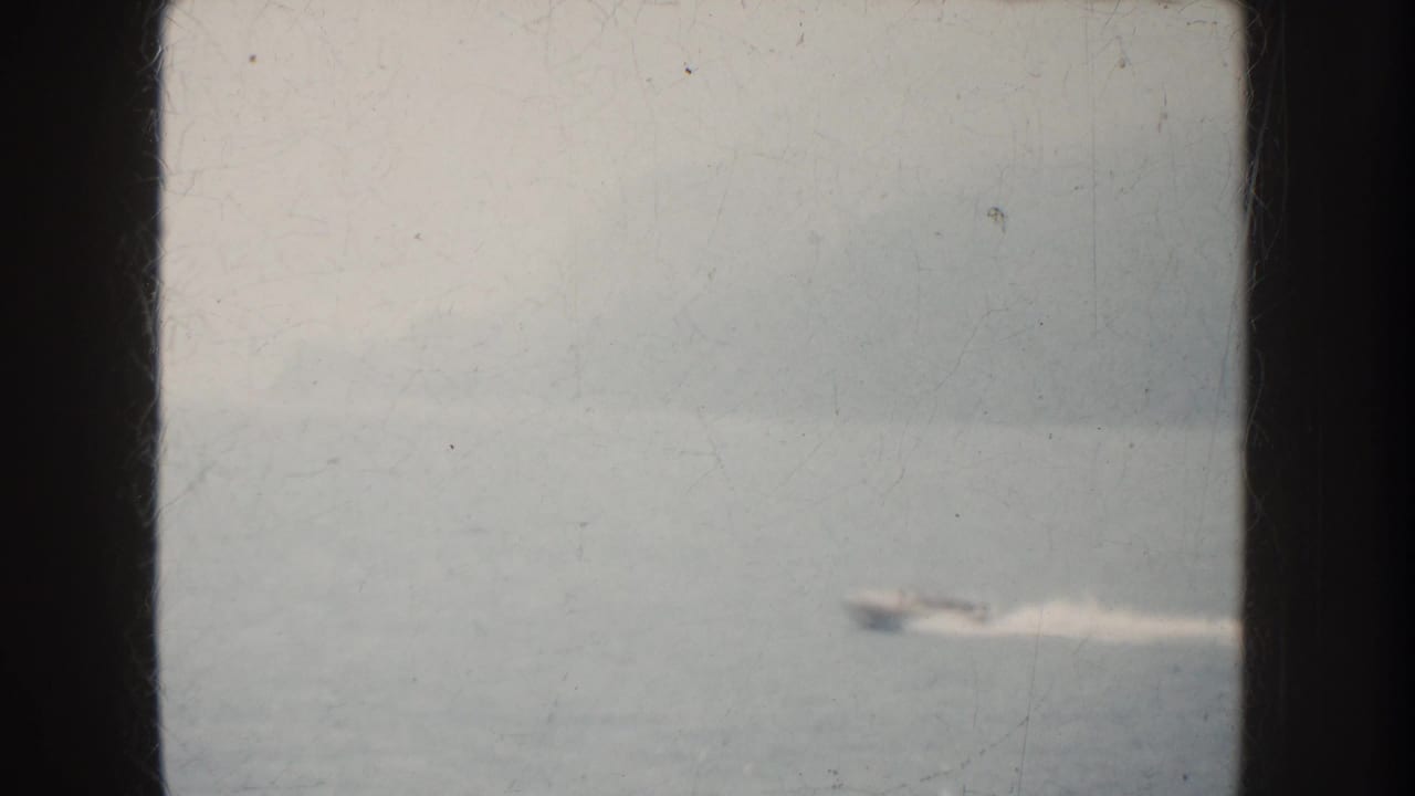 A distant motorboat appears on hazy California water, partly blurred by speed, soft focus, and aged 8mm film texture.