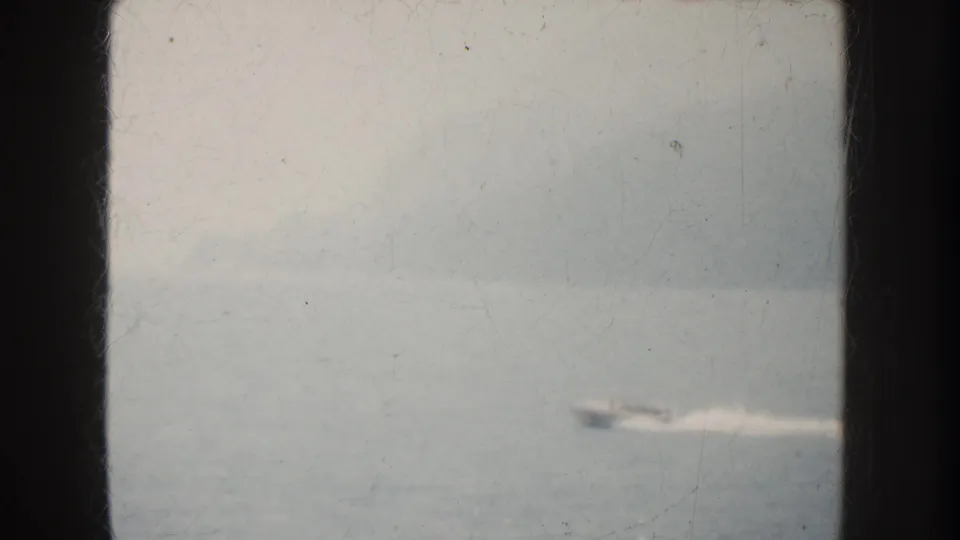 A distant motorboat appears on hazy California water, partly blurred by speed, soft focus, and aged 8mm film texture.