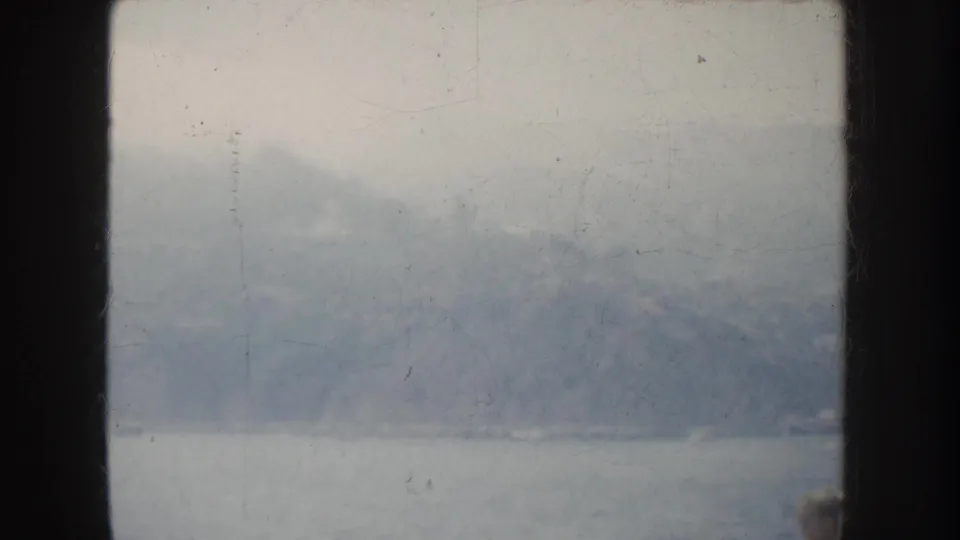 1952 California home-movie frame showing water, hazy mountains, and a partial indistinct person at lower right.